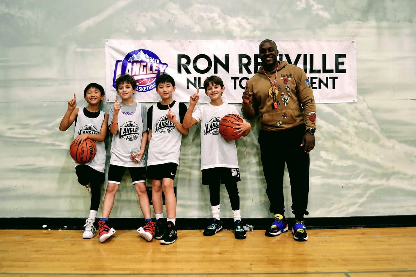 NLBA players posing with their coach in front of the Ron Renville tournament banner